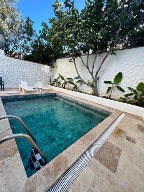 a swimming pool with two chairs next to a white wall at Doğa içinde havuzlu villa in Aydın