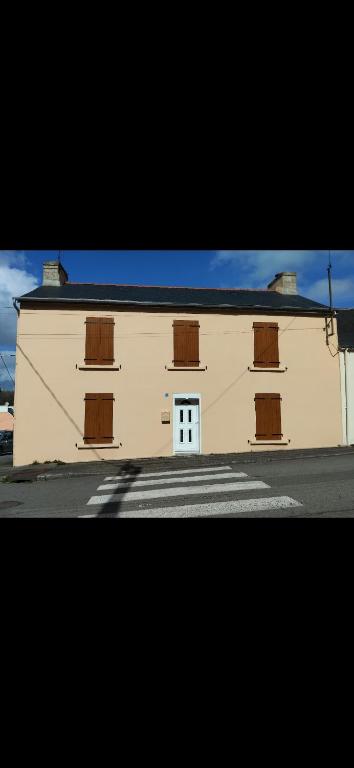 un grand bâtiment blanc avec des portes marron dans une rue dans l'établissement Maison de campagne, à Gourin