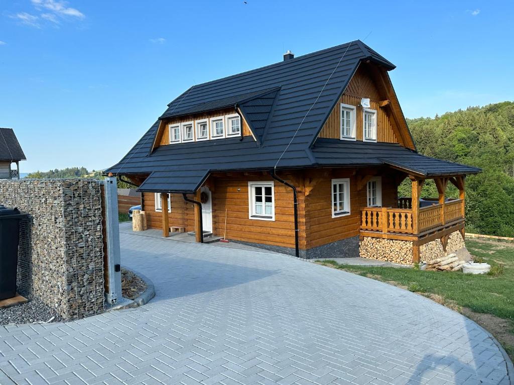 a wooden house with a black roof on a driveway at Roubenka ARCHA in Dolní Morava