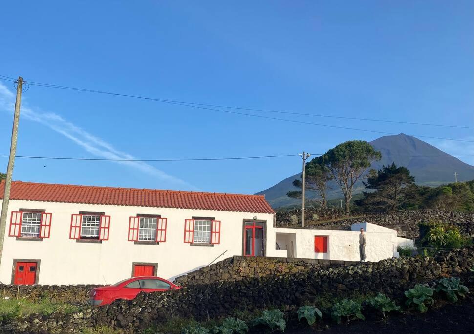 a white house with red windows and a red car in front at PicoComigo in Lajes do Pico