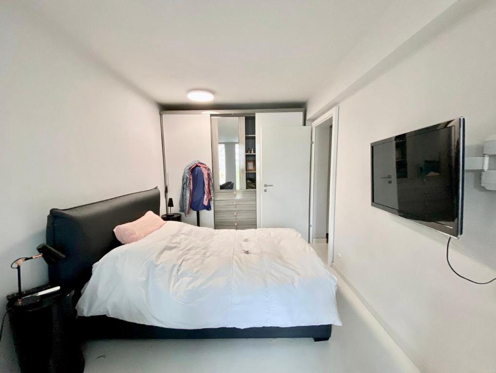 a bedroom with a white bed and a flat screen tv at NYON - Appartement meublé tout confort in Nyon