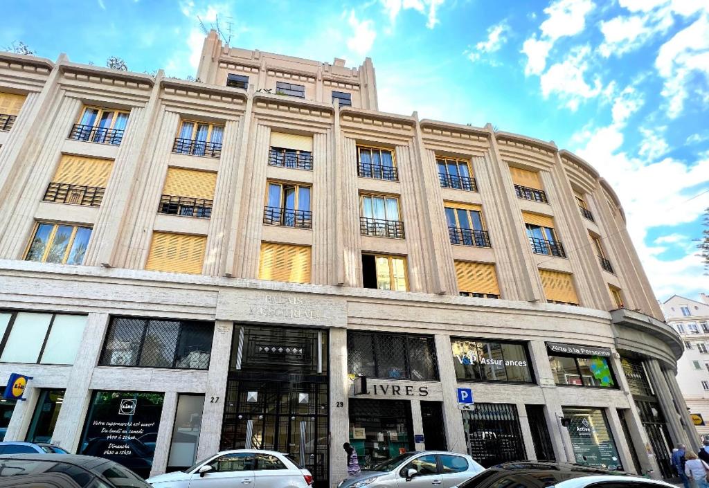 un grand bâtiment avec des voitures garées devant dans l'établissement Cosy studio ensoleillé - centre-ville – TRAM/AC, à Nice