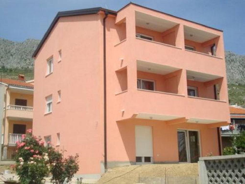 un edificio rosa con un albero di fronte di Apartments Maki a Dugi Rat (Punta Lunga)