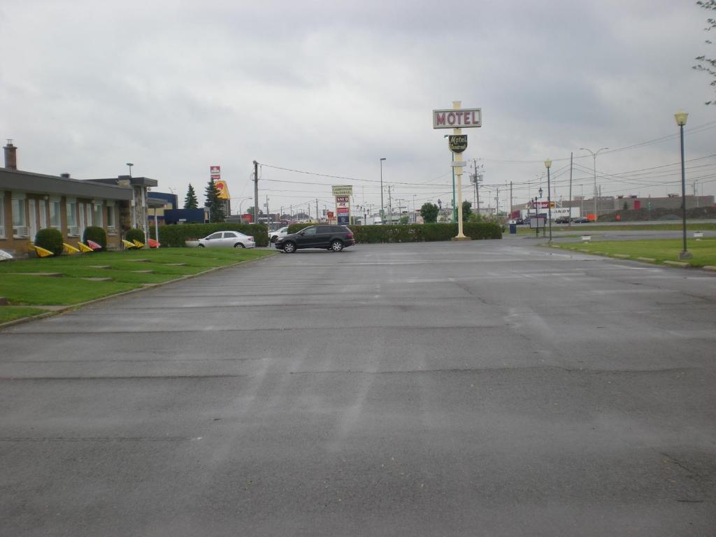 un estacionamiento vacío con un cartel de hotel y un coche en Motel Vaudreuil en Vaudreuil-Dorion