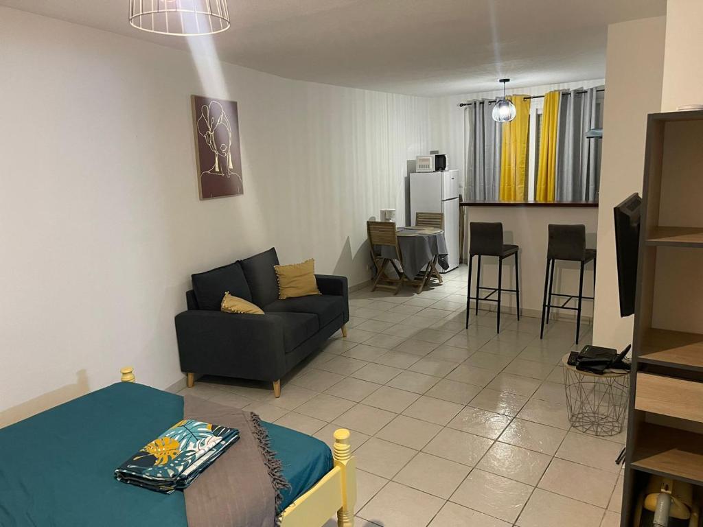 a living room with a black couch and a kitchen at Mon Cocon au Soleil in Le Lamentin