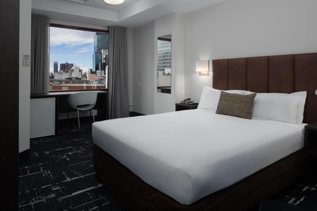 a hotel room with a bed and a desk and a window at Mercure Welcome Melbourne in Melbourne