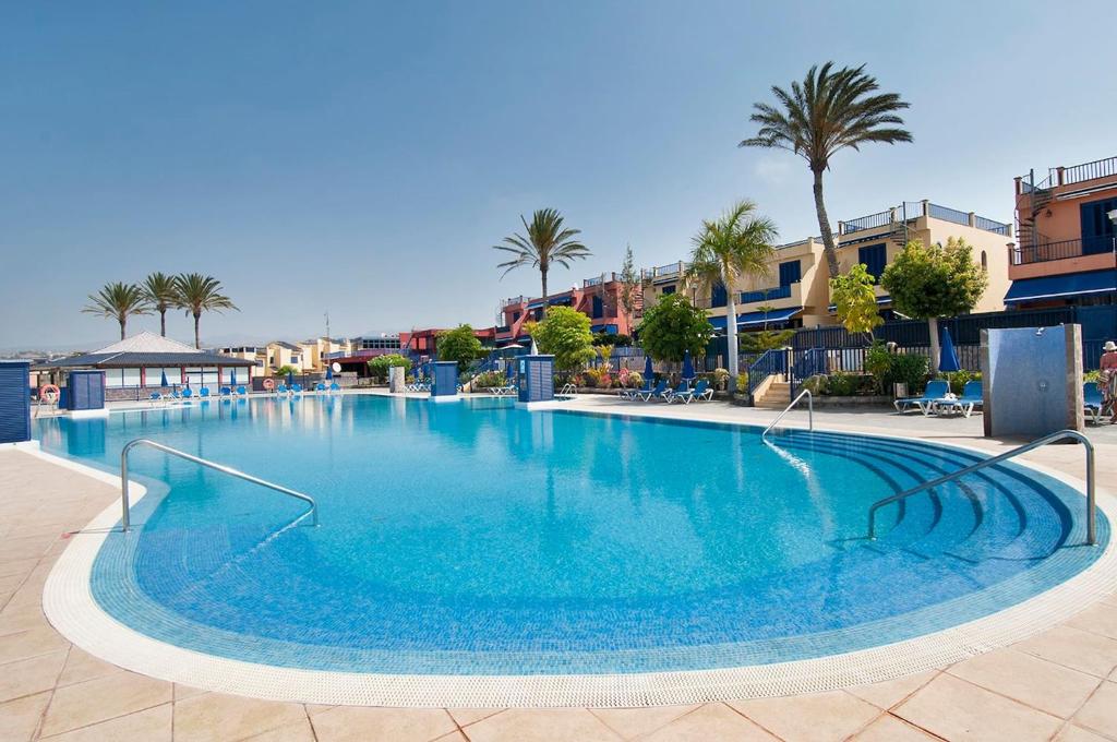 una grande piscina blu con palme e edifici di Meloneras Bay Suites a Meloneras