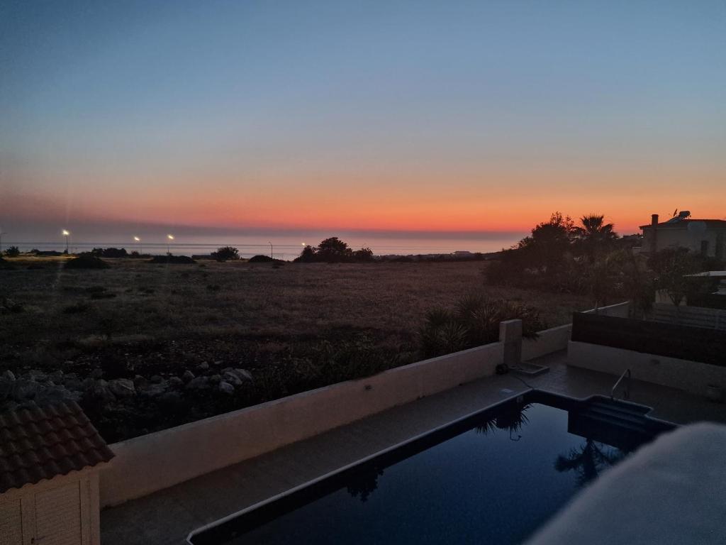 zachód słońca nad oceanem z basenem w obiekcie Villa Amavi Peyia w Pafos
