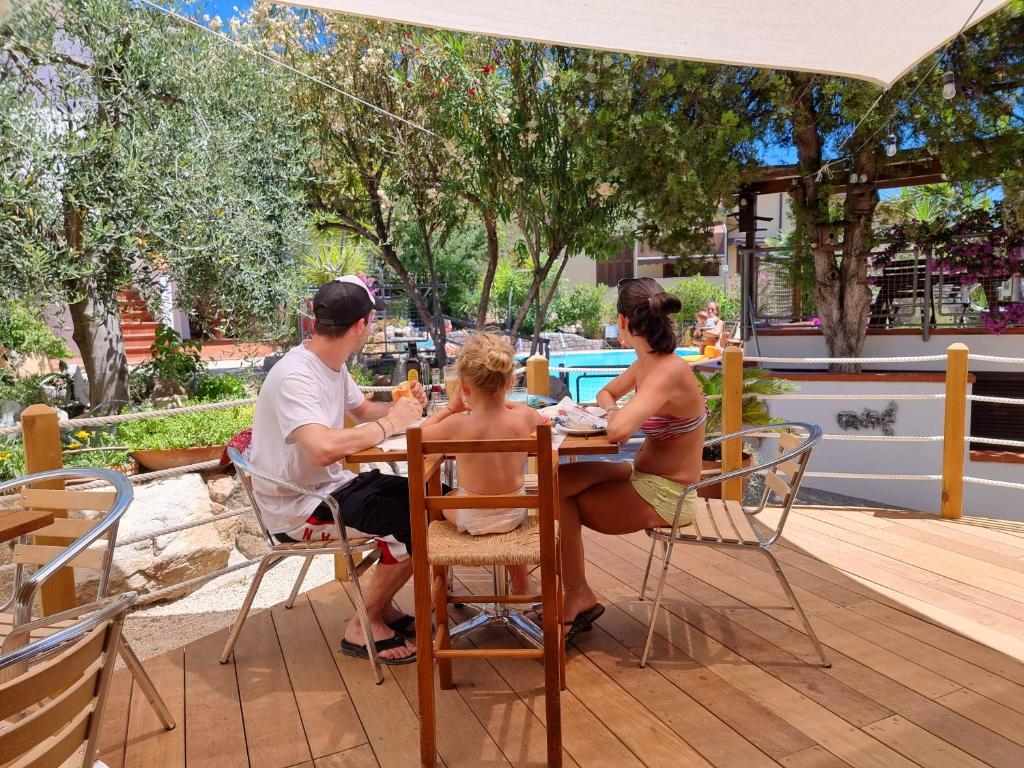 a group of people sitting at a table under an umbrella at Eco Hotel Montemerlo in Fetovaia