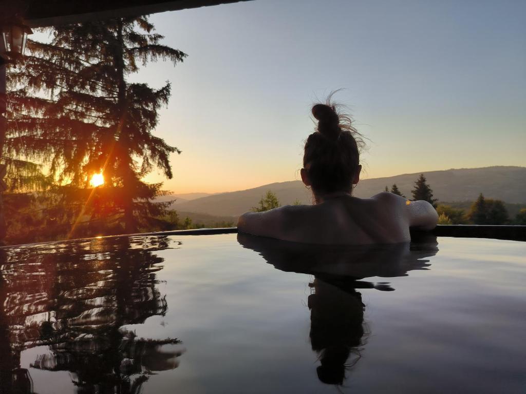 een vrouw zittend in een overloopzwembad bij zonsondergang bij Alpina Panoramic in Moisei