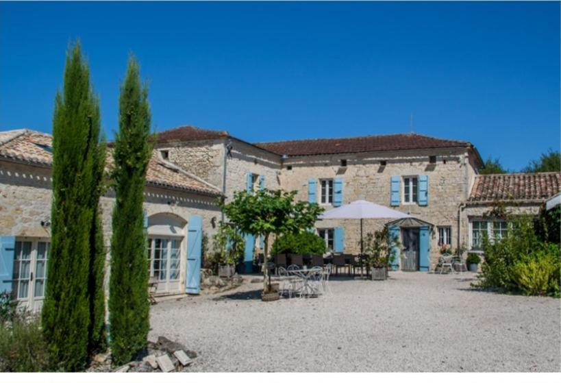 a large stone building with a patio and umbrella at La nouvelle vie en Quercy in Montaigu-de-Quercy