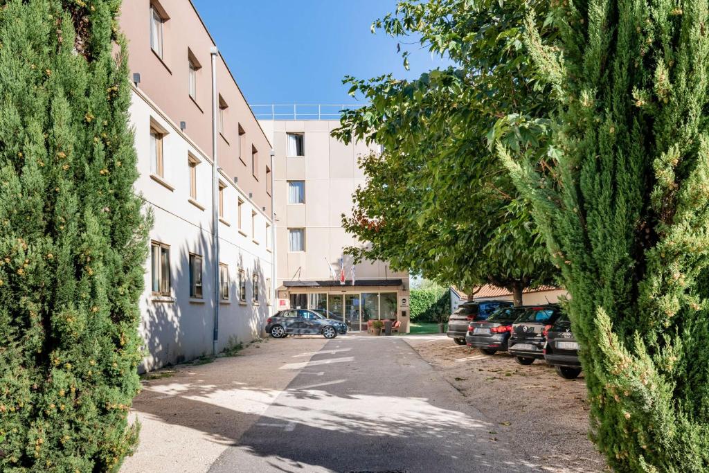 een straat met een gebouw en auto's geparkeerd aan de zijkant bij Best Western Hôtel des Barolles - Lyon Sud in Brignais