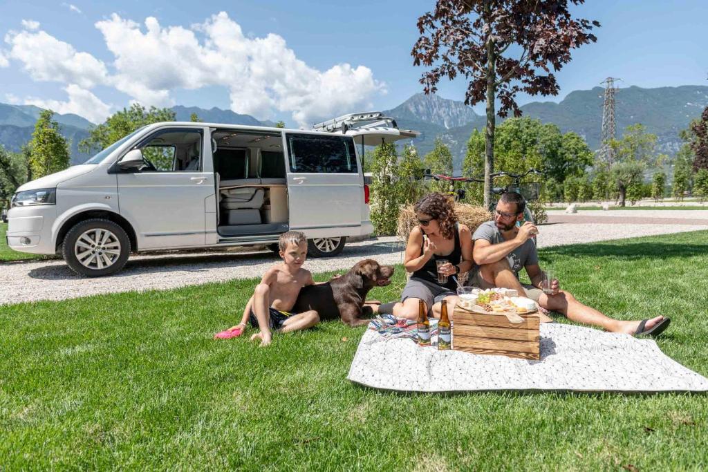 a group of people sitting in the grass with a dog at Camping Agrisalus in Arco