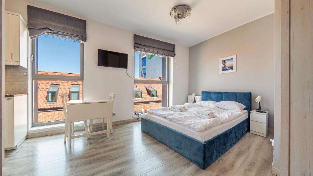 a bedroom with a bed and a desk and windows at Apartamenty Sun & Snow Deo Plaza Granaria in Gdańsk