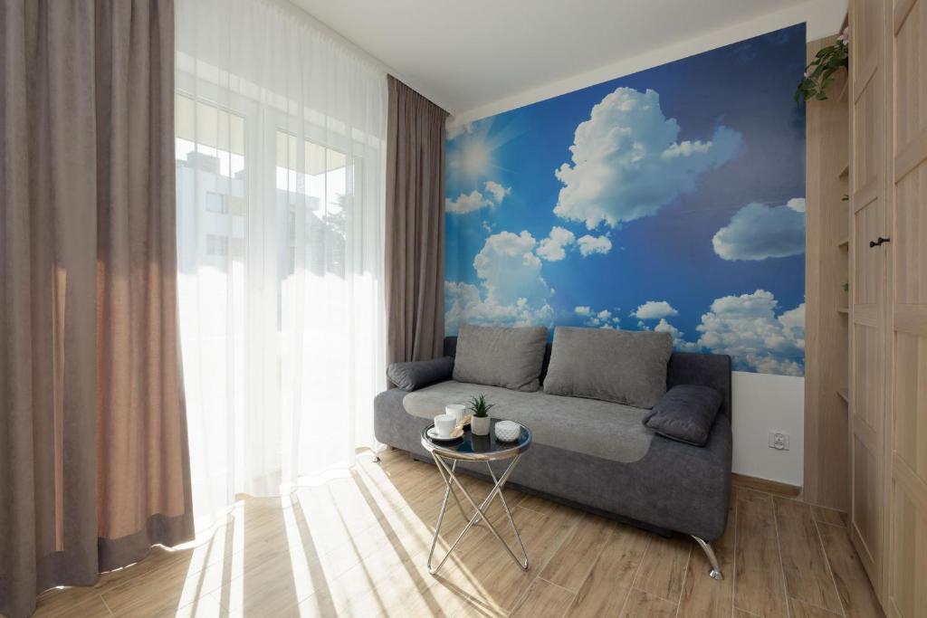 a living room with a couch and clouds mural at Klimaty Bałtyku Studio with Terrace & Parking in Dziwnów by Renters in Dziwnów