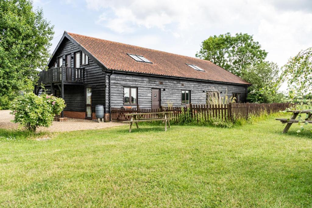 a large wooden building with a fence and picnic tables at The Dairy - Holly Tree Barns in Halesworth