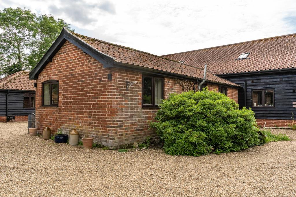 a brick house with a bush in front of it at The Stables - Holly Tree Barns in Halesworth