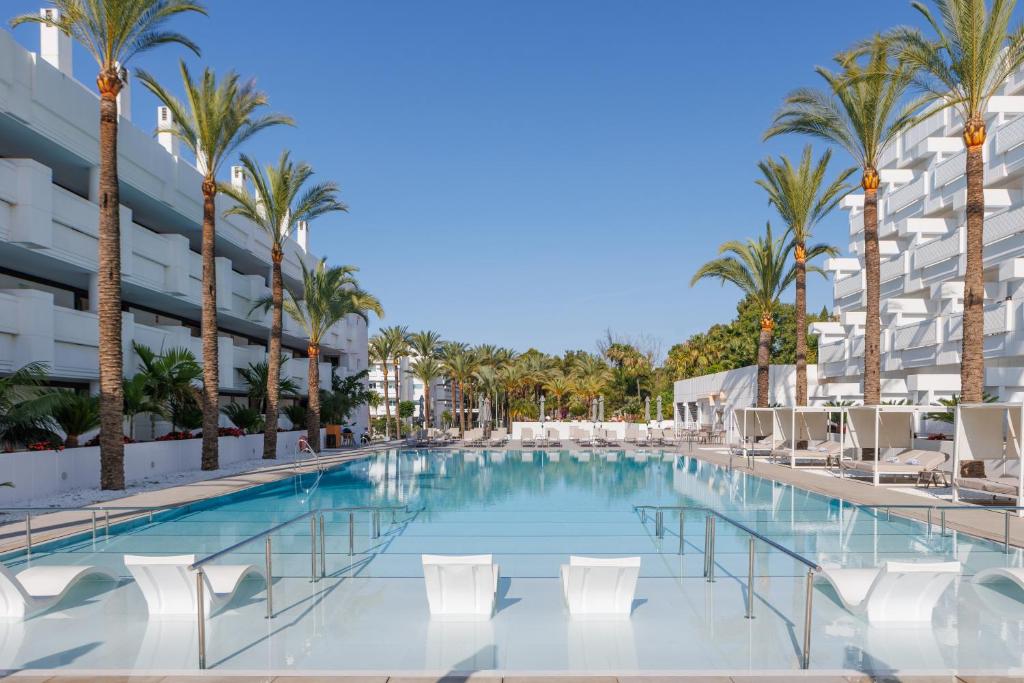 a swimming pool with chairs and palm trees in front of a building at Alanda Marbella Hotel in Marbella