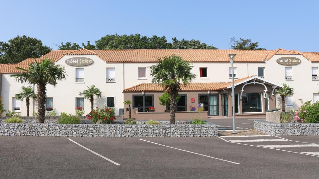 a large white building with palm trees in a parking lot at Hotel Salea in Pornic