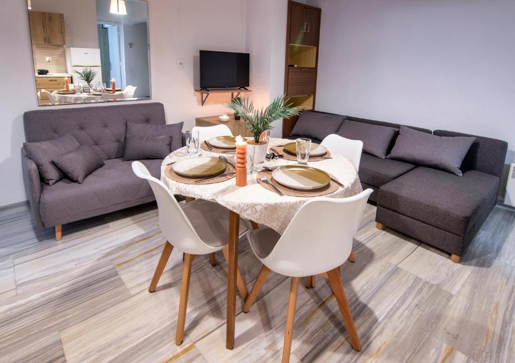 Anali Apartment في إيكسيا: طاولة طعام مع كراسي بيضاء وأريكة