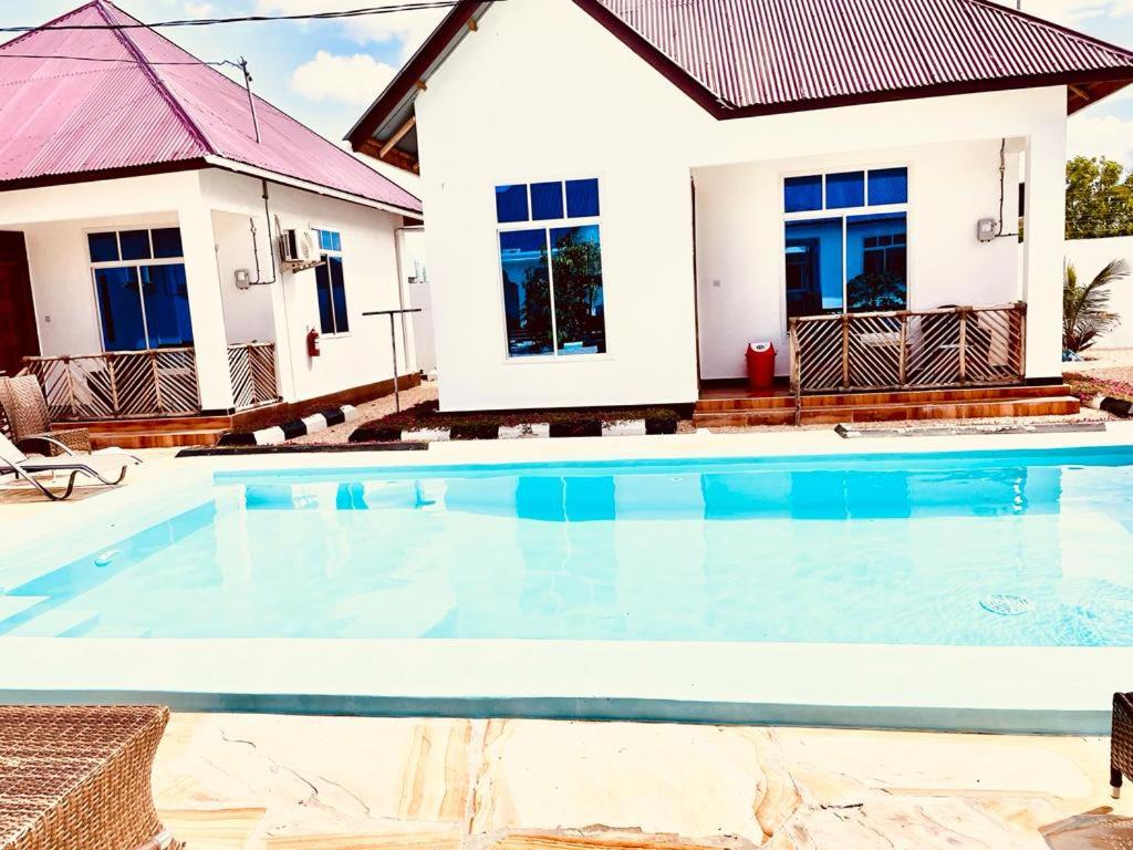a villa with a swimming pool in front of a house at Mbuyu Uvi Apartment in Paje