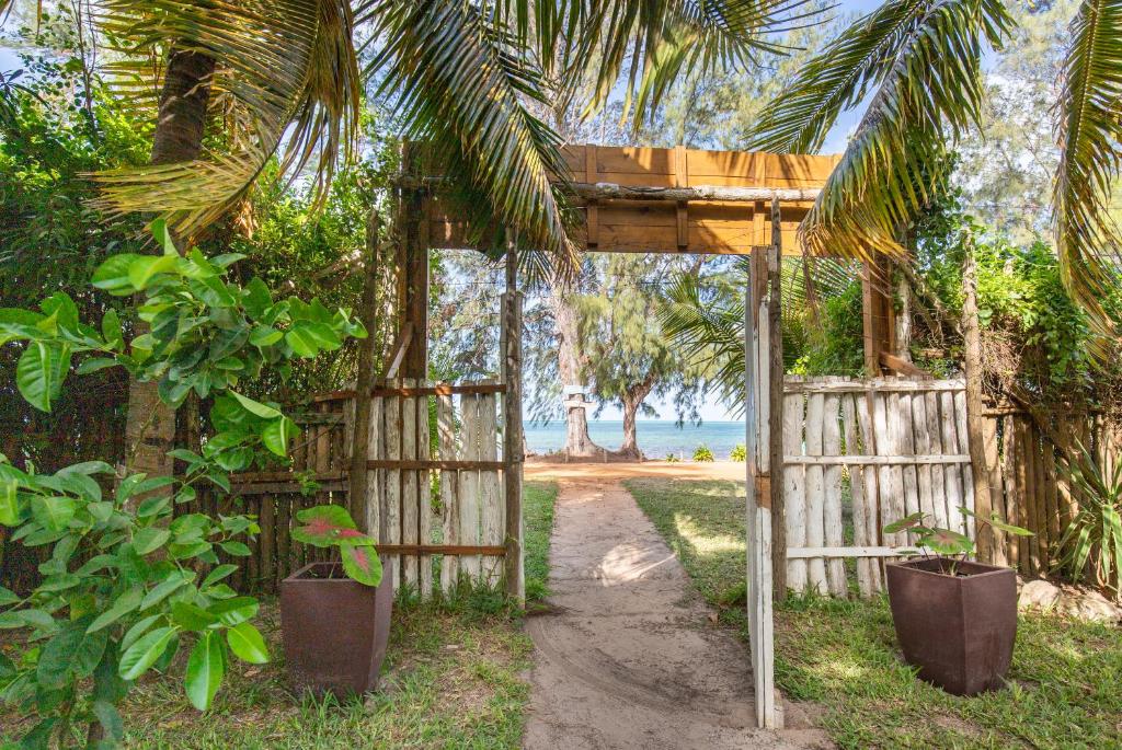 a wooden gate and a fence with trees and the ocean at LEMON BEACH LODGE Vilankulo in Vilanculos