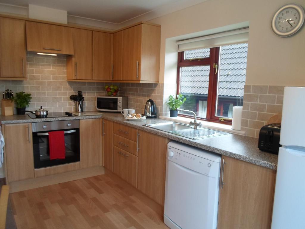 a kitchen with wooden cabinets and a white dishwasher at Alpine Park Cottages in Aylesbeare