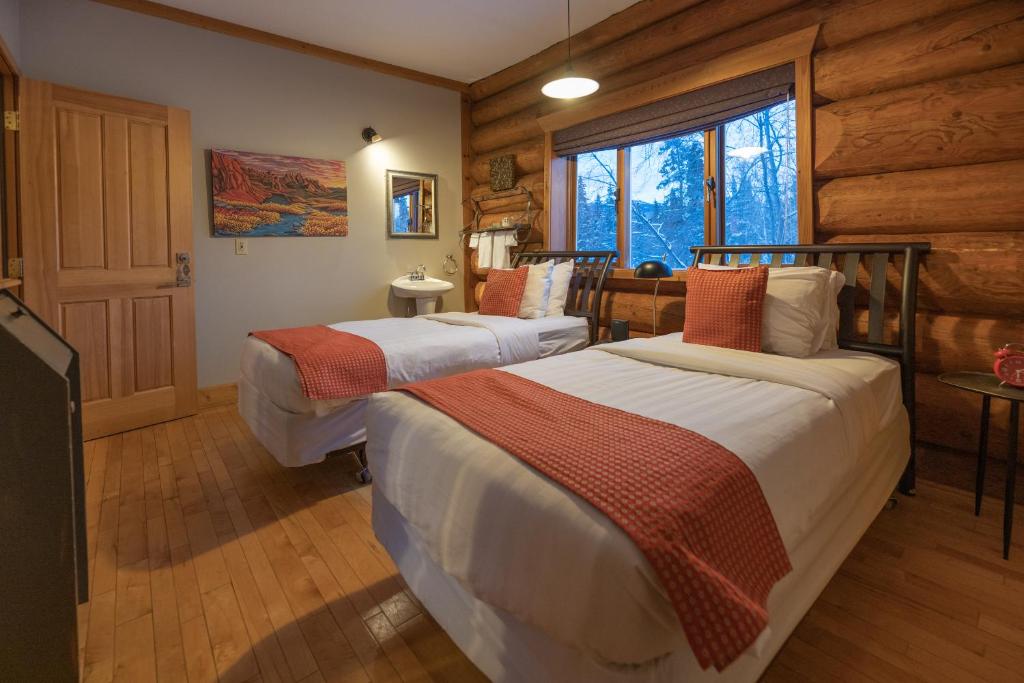 two beds in a room with wooden walls at Inn on the Lake - Whitehorse in Marsh Lake