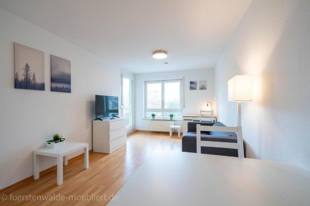 uma sala de estar branca com um sofá e uma televisão em 2 Zimmer mit Balkon, Wohnzimmer mit Arbeitsplatz, zentral, top! em Fürstenwalde
