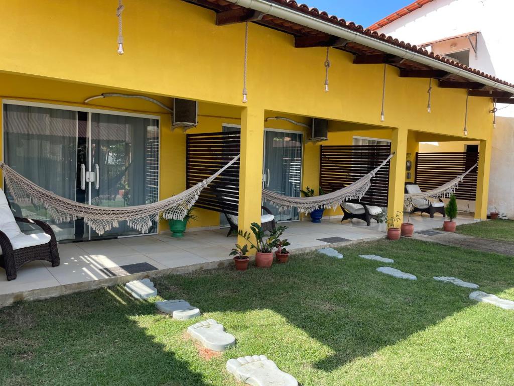 a yellow house with hammocks on a patio at Casa Temporada Suítes in Maragogi