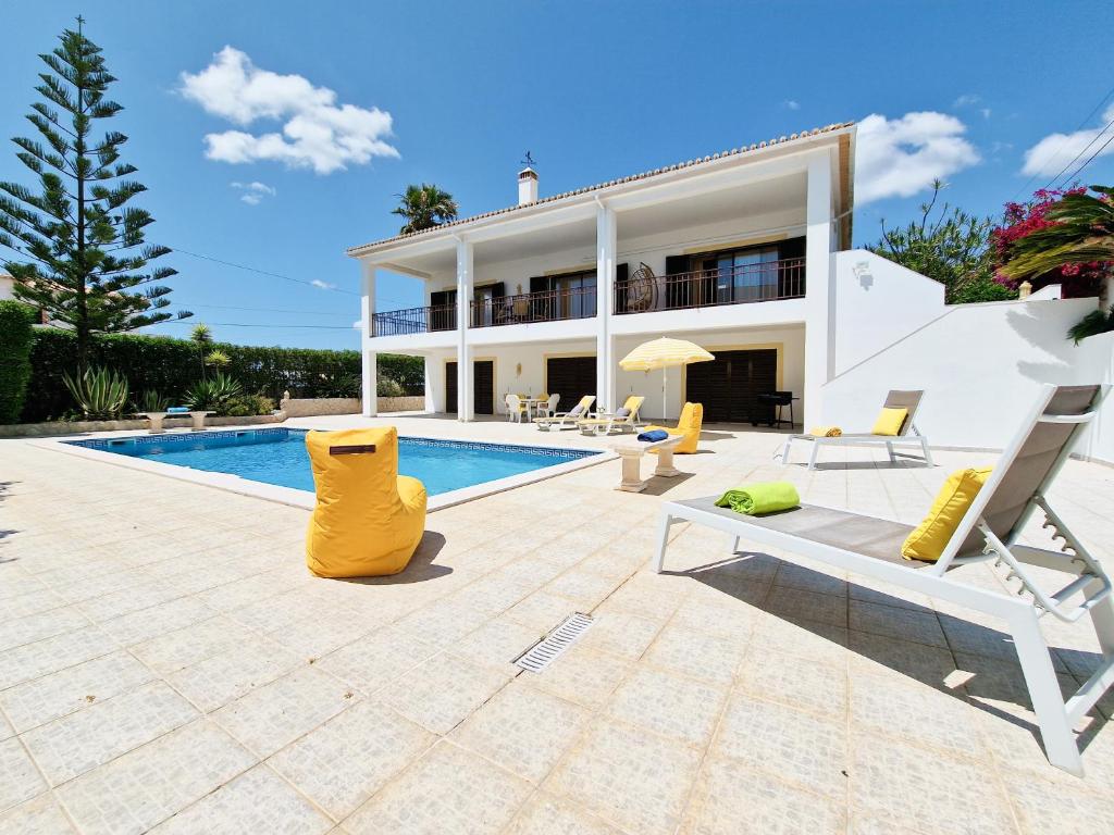 a villa with a swimming pool with yellow chairs at Villa Ninho do Mocho in Portimão