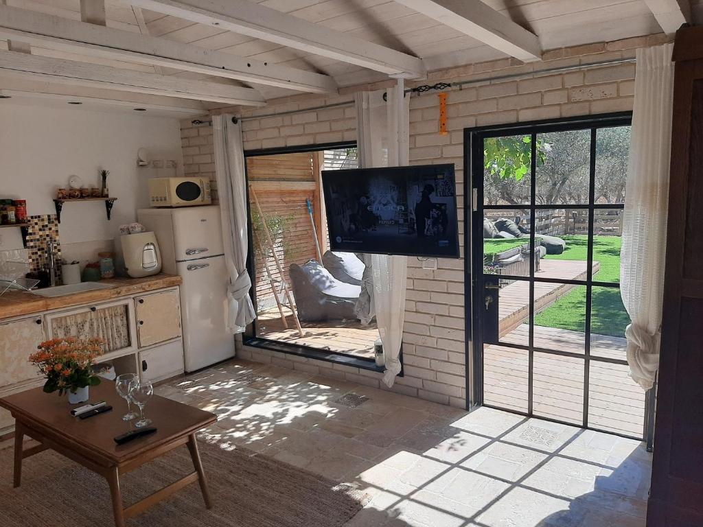 a living room with a television and a kitchen with a sliding glass door at בשרונה בגליל in Sharona