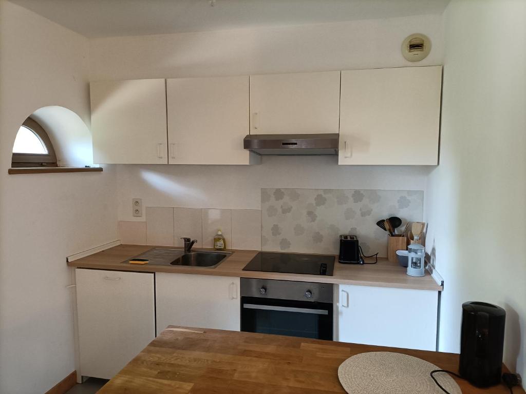 a kitchen with white cabinets and a sink and a table at La Jolie Dourbie de Nant in Nant