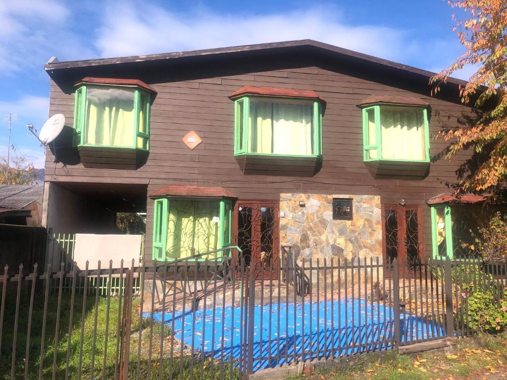 una casa con ventanas verdes y una valla en Hostel Huepil, en Pucón