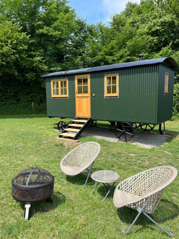uma cabana verde com duas cadeiras e um grelhador na relva em Troytown Farm Shepherds hut em Puddletown