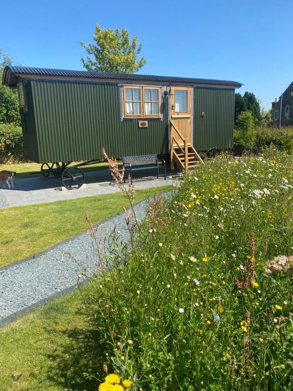 a green tiny house in a garden with flowers at Woody's Retreat in Bolton by Bowland