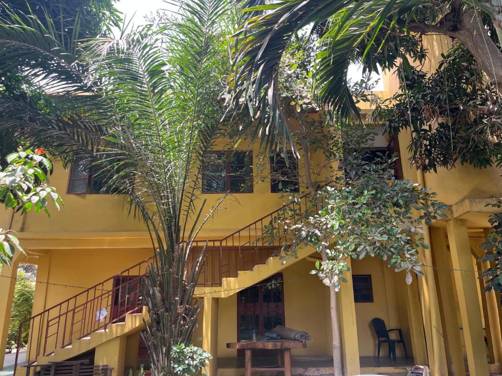 a yellow building with palm trees in front of it at Boli Boli Guesthouse in Sere Kunda