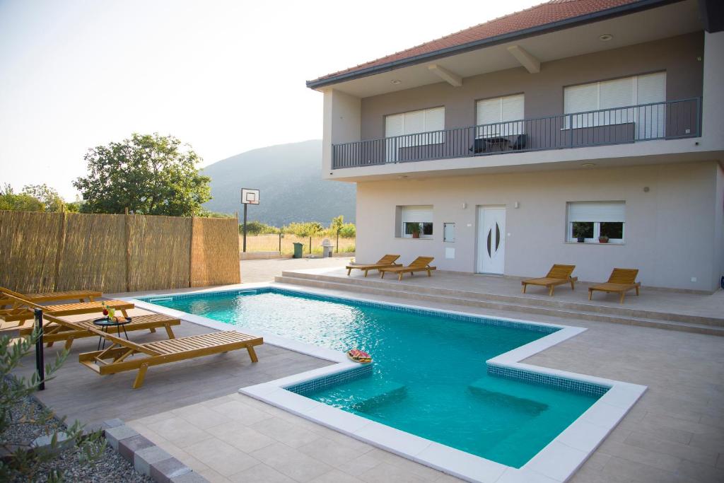 a swimming pool with benches and a house at Villa Village Mostar in Mostar