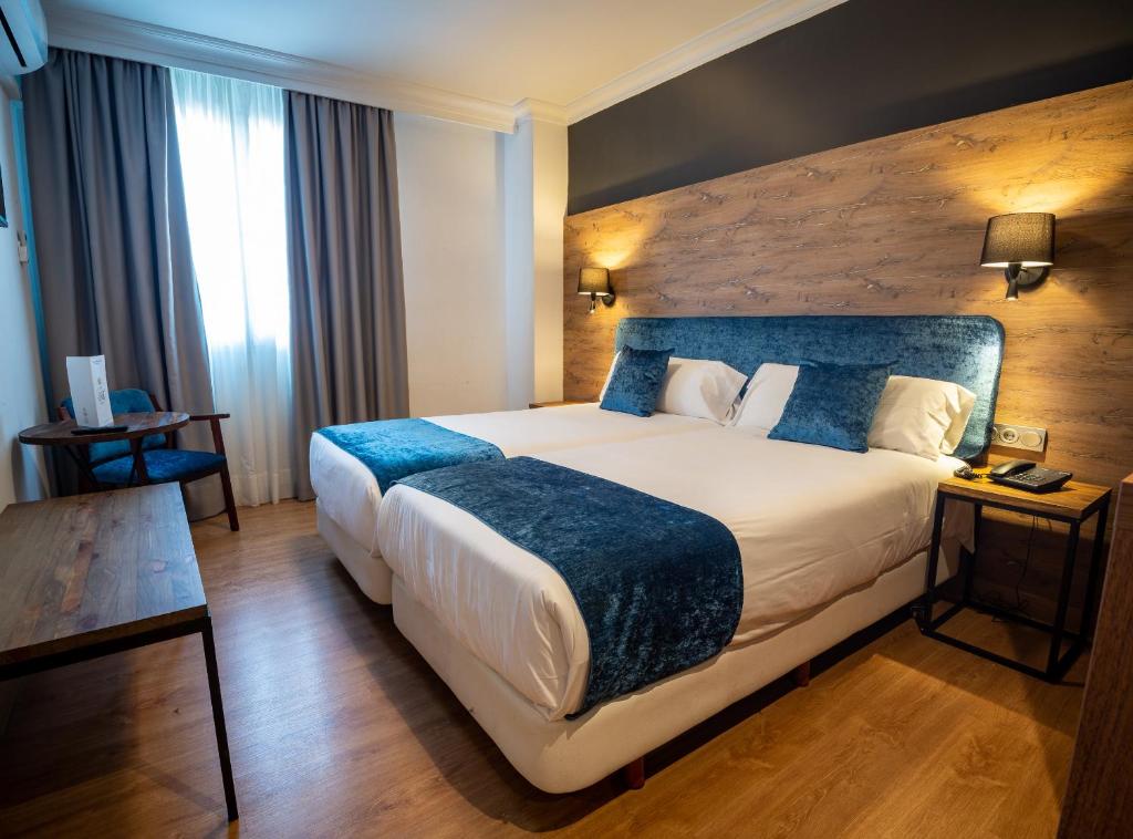 a hotel room with a large bed with a blue blanket at Hotel Familia Conde in Huelva