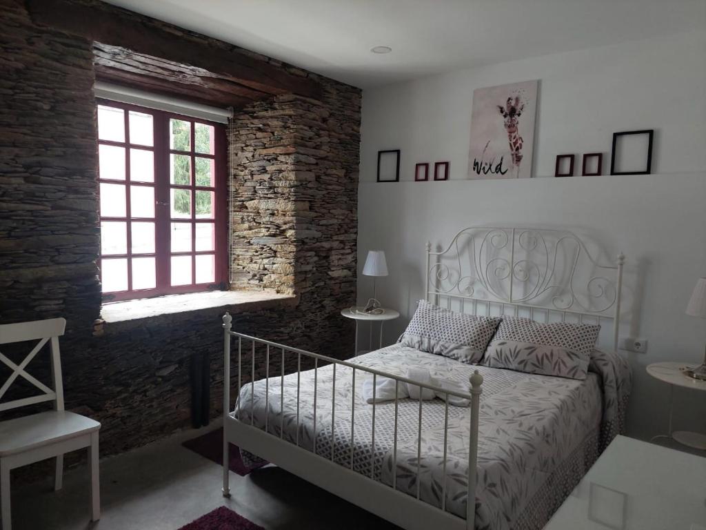 um quarto com uma cama branca e uma parede de tijolos em ALBERGUE CASTELOS em Lorenzana