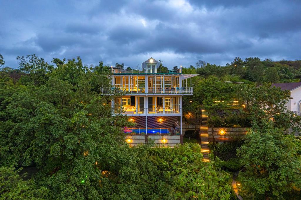 a large building with lights in the trees at The Glasscape by StayVista - Hillside getaway with Pool and Indoor games in Nashik