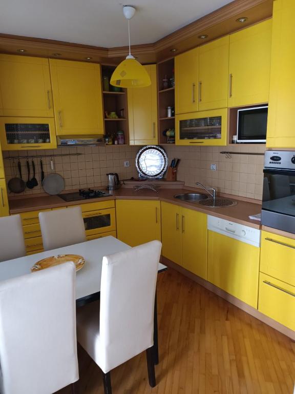 a kitchen with yellow cabinets and a white table and chairs at Apartman Nodi in Sarajevo