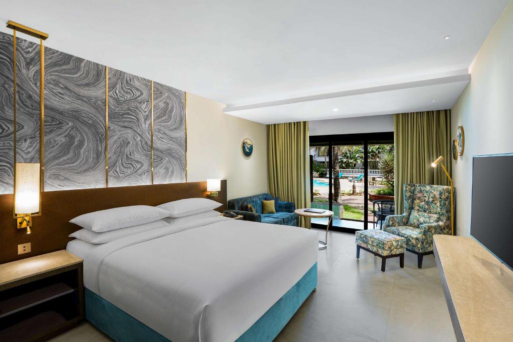 a hotel room with a large bed and chairs at DoubleTree by Hilton Hotel Goa - Arpora - Baga in Baga