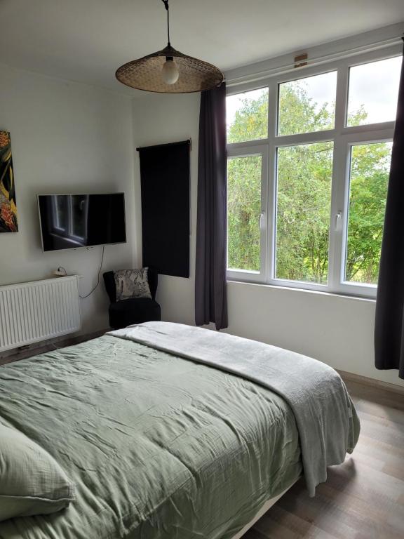 um quarto com uma cama grande e 2 janelas em La Maison des Roses em Francorchamps