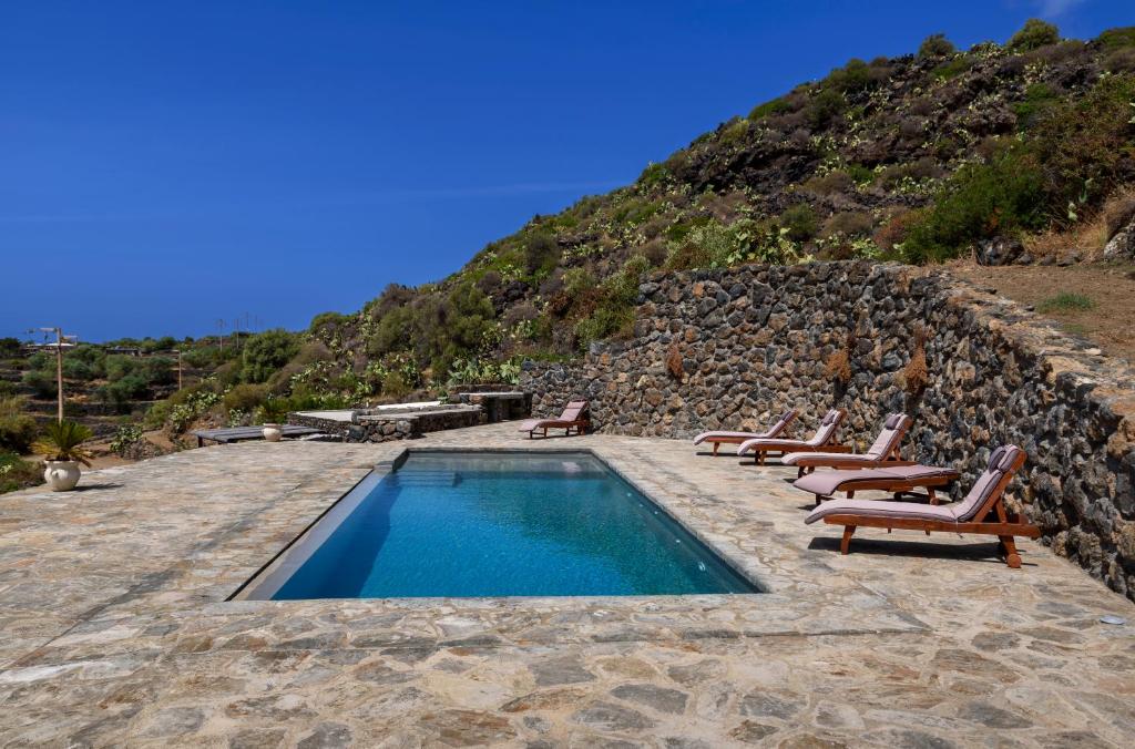 a swimming pool with lounge chairs and a rock wall at Agriturismo Zibibbodoro in Pantelleria