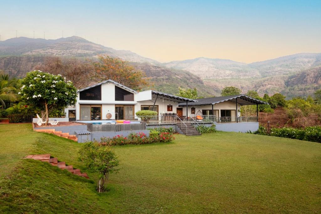 a house with a large yard with mountains in the background at SaffronStays Sanvina Farm, Karjat in Karjat