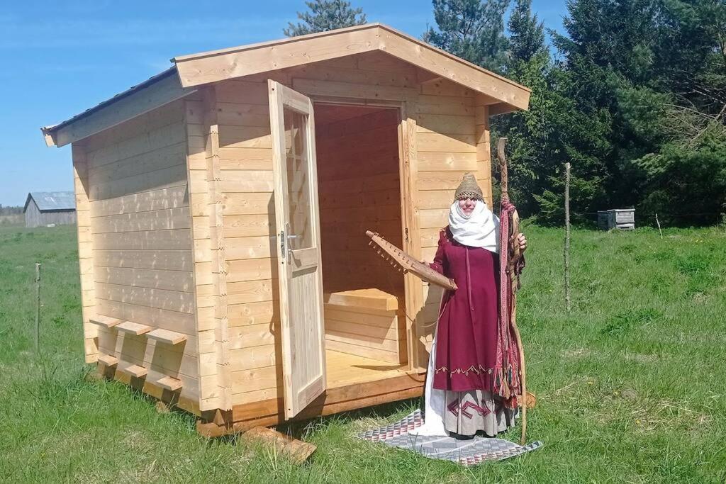 une femme debout devant un hangar en bois dans l'établissement Bičių lova. Bičių terapija. Bee bed. Bee therapy, 