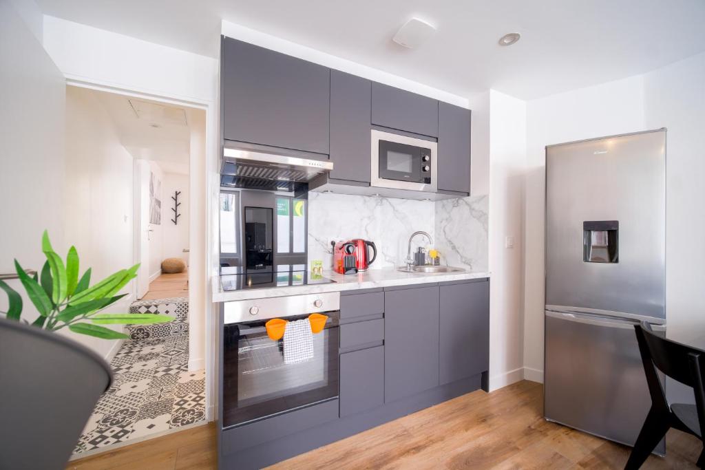 a kitchen with gray cabinets and a stainless steel refrigerator at Idyllique T2 tout confort avec sa terrasse ensoleillée in La Ferté-Gaucher