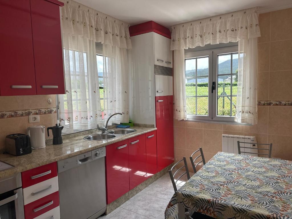 eine Küche mit roten Schränken, einem Tisch, einem Tisch und einem Fenster in der Unterkunft Casa ceferino in Barreiros