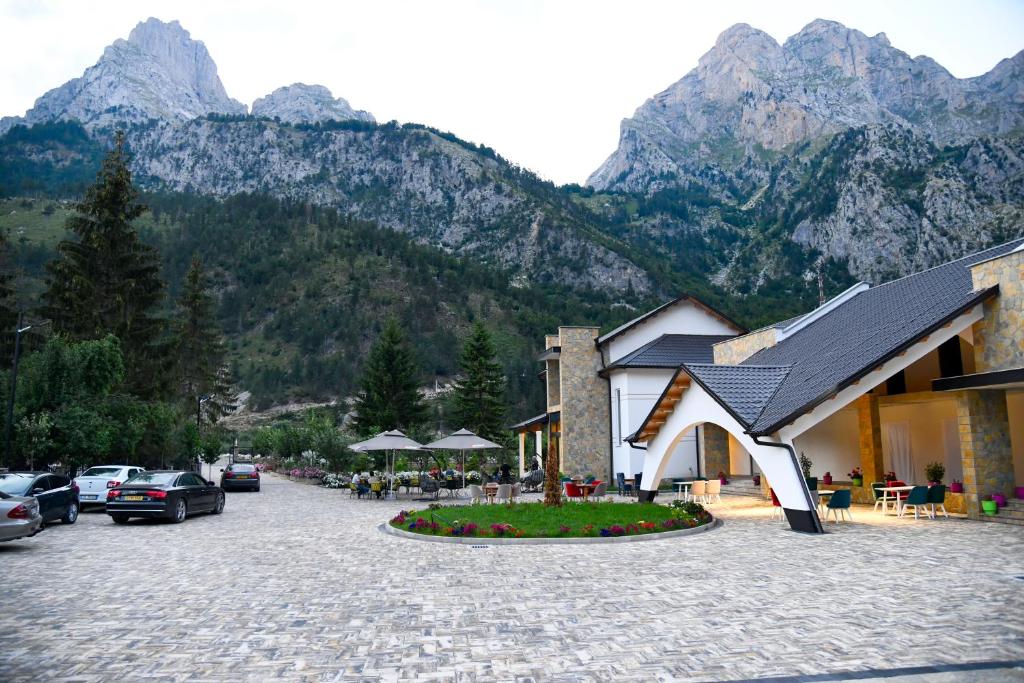 a building with cars parked in a parking lot with mountains at Breezy Hotel in Valbonë